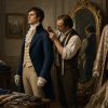Late-18th-century gentleman in a dark navy tailcoat being fitted by a tailor, with a richly embroidered silk coat nearby to contrast restrained tailoring with ornate dress.