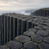 Generated geological illustration of dark basalt columns beside an overcast ocean, showing adjoining irregular polygonal tops in the foreground and tall joint-bounded sides along the cliff.