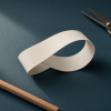 AI-generated illustration of an ivory paper Möbius-strip model resting on a dark teal desktop, with a wooden pencil at lower left and black-handled scissors at upper right; the ribbon curves through a half-twist.