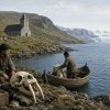 Norse Greenland walrus hunters prepare tusks for a distant medieval trading ship beside a fjord and turf-roof settlement.